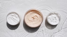 A jar of white cream on a water surface. Splash of water, sunlight and shadows. Layout for advertising goods, cosmetic products. Medical skin care, body care. - Powered by Shutterstock - Get 15% off with code: PIKWIZARD15
