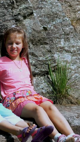 Two pretty girls, kids, sit on a ledge in the rock., a beautiful orange mountain butterfly whirls and flies over a child