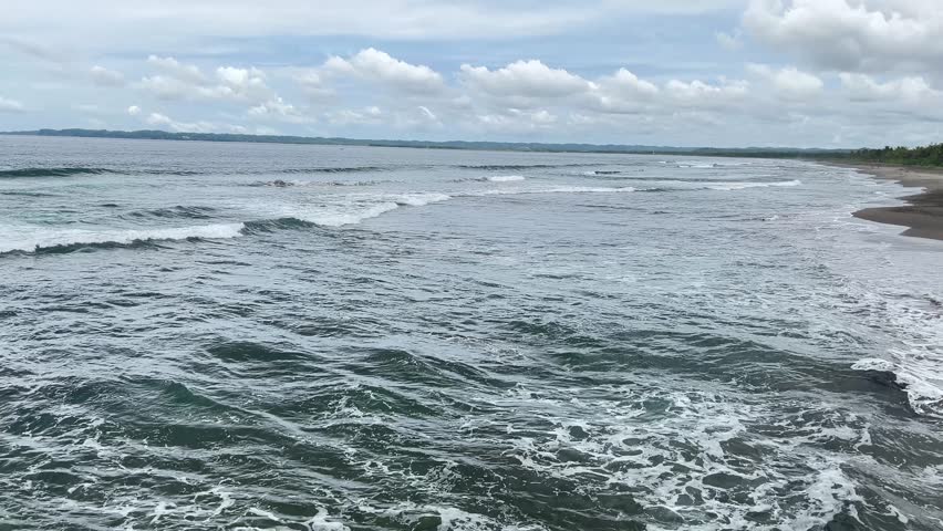 Wide View of Choppy Ocean Waves Crashing onto a Long Beach Shoreline