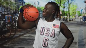 Man holding basketball on shoulder in street wearing usa white jersey with flag patch and blue wristbands, smiling and looking down at ball; team pride. - Powered by Shutterstock - Get 15% off with code: PIKWIZARD15