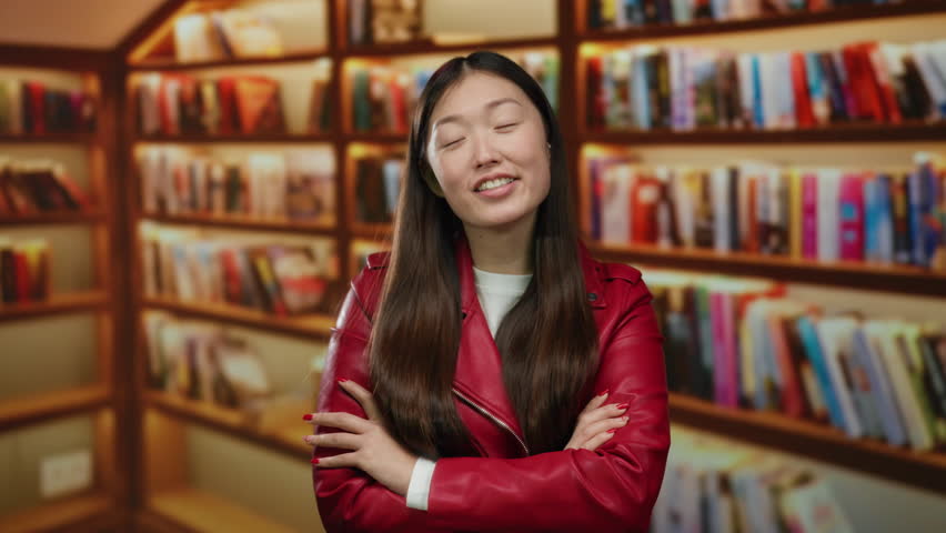 Woman standing confidently in a library wearing a red jacket with books lining the shelves conveying knowledge and learning in an academic indoor setting in china featuring asian beauty