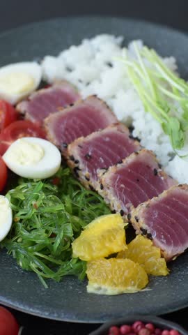 Seafood bowl, tuna tataki fillet slices with rice, oranges, tomatoes and sauce. Tuna bowl as a food background for your design
