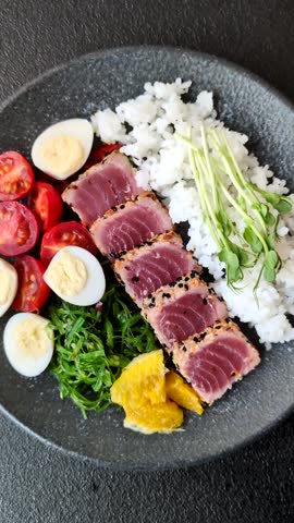 Seafood bowl, tuna tataki fillet slices with rice, oranges, tomatoes and sauce. Tuna bowl as a food background for your design