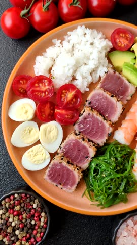 Seafood bowl, tuna tataki fillet slices with rice, oranges, tomatoes and sauce. Tuna bowl as a food background for your design