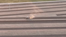 High aerial view of a farm tractor plowing the dry soil and creating furrows in a vast agricultural field, kicking up clouds of dust as it prepares the land for a new crop season - Powered by Shutterstock - Get 15% off with code: PIKWIZARD15