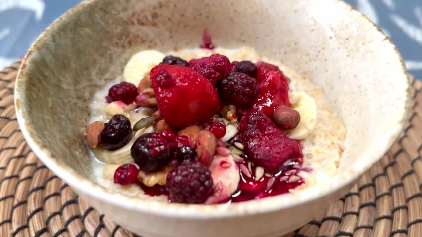 nuts being poured into healthy bowl of porridge with milk berries and banana