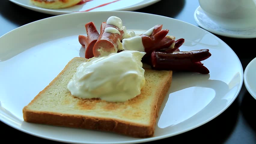 Video footage of various dishes from a traditional continental breakfast on a table. Fried sausages, poached eggs, and pancakes with sour cream and jam on plates at restaurant 
