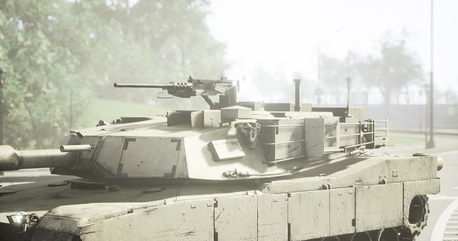 A military tank maneuvers quietly down a city street shrouded in early morning fog. The environment appears calm as the vehicle moves past streetlights and trees in the background.