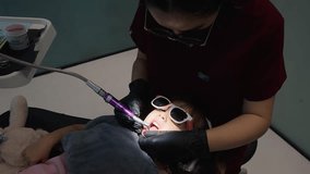 Experienced female dentist providing dental care to a young girl. The patient is comfortably reclined in the dental chair wearing safety glasses while receiving treatment - Powered by Shutterstock - Get 15% off with code: PIKWIZARD15