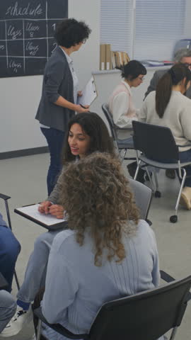 Adult Students Divided Into Two Separate Discussion Circles. Teacher Moves Between Groups, Observing Progress, Offering Feedback, Engaging in Short Conversations About Assignment. Vertical Shot.