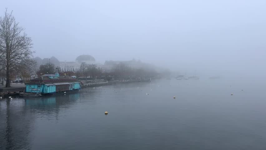Zurich, Switzerland. November 5, 2025. Foggy Zurich Lake. The camera pans from right to left. On the left side of the shore, you can see the Zurich Opera House.