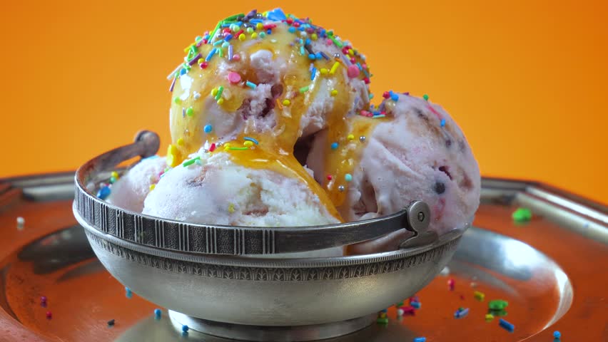 Vanilla ice cream in a metal bowl sprinkled with edible confetti slowly rotates against a bright background.