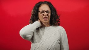 Woman with curly hair in sweater expressing neck pain against vivid red background looking distressed and uncomfortable. - Powered by Shutterstock - Get 15% off with code: PIKWIZARD15