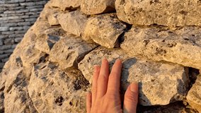 A close-up shot of a hand touching an old stone wall under warm natural sunlight. The textured stones and soft golden light create an atmosphere of history, nature, and tactile connection.  - Powered by Shutterstock - Get 15% off with code: PIKWIZARD15