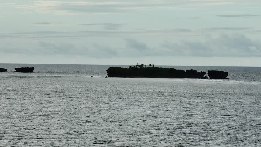 Rocky island in the sea with palm trees on top surrounded by calm water. Siargao, Philippines.