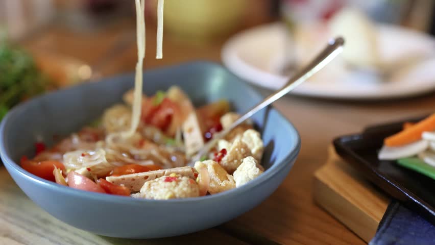 Close-up of spicy Thai noodle salad with tofu, tomatoes, and chili in natural restaurant lighting