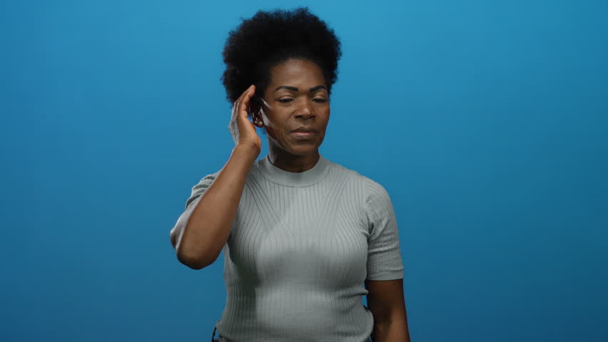 Woman expressing surprise holding hand to her ear on a blue isolated background capturing emotion and curiosity