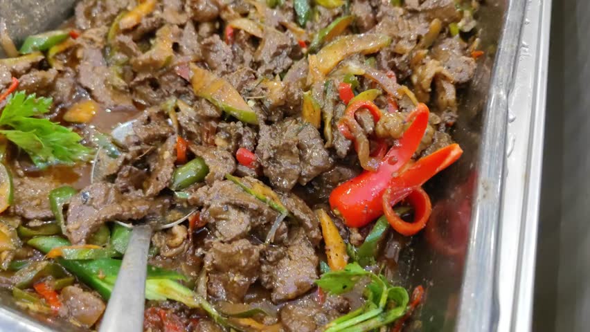 A close-up shot of spicy sautéed beef cooked with sliced chilies, onions, and mixed vegetables. The dish appears rich, savory, and oily with a variety of colors from red chili, green chili, and aromat