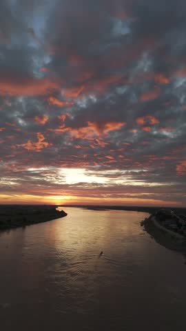 Warm sunrise over Mekong River with dramatic sky, calm water reflections, traditional boats and peaceful Thai riverside atmosphere in early morning light.