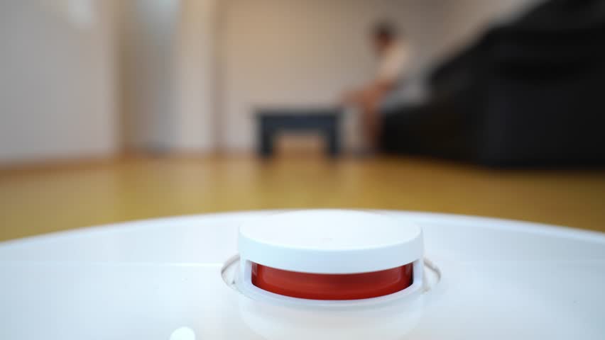 Close-up shot of a smart robot vacuum cleaner with a lidar sensor in a modern living room. Automated cleaning device with a blurred person in the background, illustrating home automation, convenience 