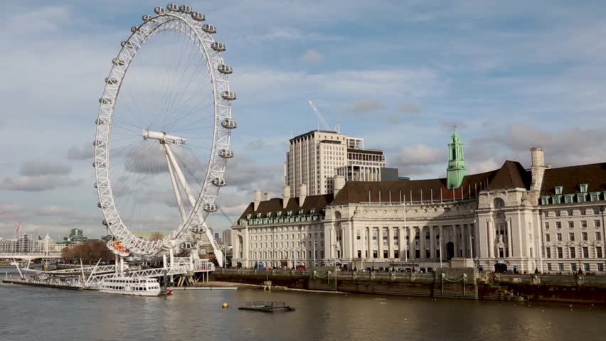 Stunning wide-angle shot of the London Eye against a bright sky, overlooking the Thames River. Captures vibrant city life, iconic architecture, and bustling riverbank on a clear day.