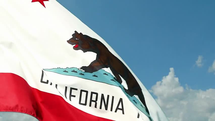 Slow-motion timelapse of the California state flag waving against a blue sky with clouds, symbolizing state pride, governance, and Americana.