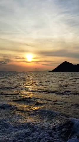 Sunset over the ocean with a mountain silhouette and water movement from a boat.