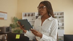 African american woman holding a tablet and smiling while standing at a desk in an office wearing glasses; confidence productivity. - Powered by Shutterstock - Get 15% off with code: PIKWIZARD15