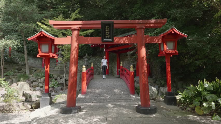 Young caucasian woman walking through red torii gate and over red bridge in Beppu Hells, Japan.