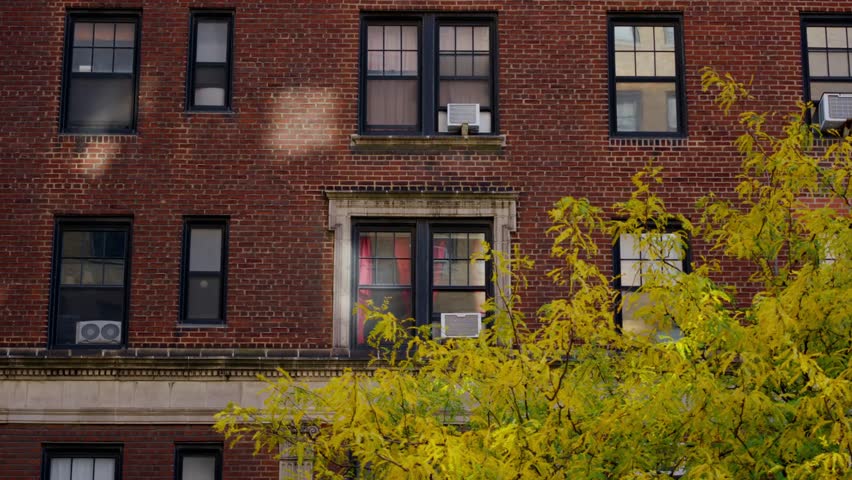 Autumn scene of a traditional red brick apartment building with yellow leaves in front yard, NYC, New York, United States