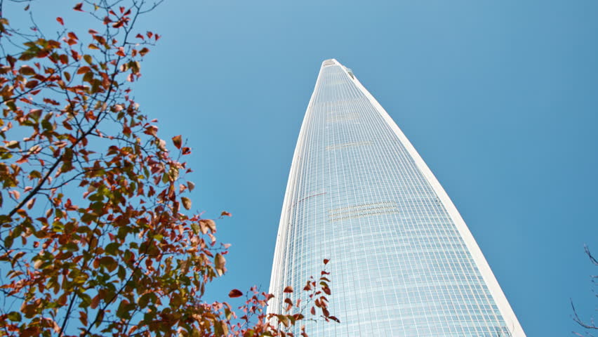 A Tall Modern Skyscraper Standing Against a Clear Blue Sky, Surrounded by Vibrant Autumn Leaves in Seoul, South Korea, Natural Light