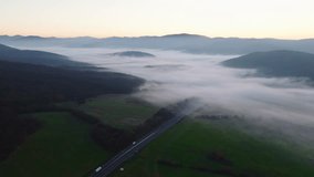 Aerial view of a fog-filled mountain valley at dawn, with soft light illuminating rolling hills, open fields, and a road cutting through the misty landscape. - Powered by Shutterstock - Get 15% off with code: PIKWIZARD15