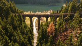 Aerial view of the Telgárt stone railway viaduct in Slovakia, surrounded by dense forest and warm sunlight highlighting the arches and valley path below. - Powered by Shutterstock - Get 15% off with code: PIKWIZARD15