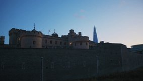 The Tower of London’s stone battlements stand in twilight, with the Union Jack flying above and a skyscraper rising in the background, contrasting medieval fortification with modern London skyline. - Powered by Shutterstock - Get 15% off with code: PIKWIZARD15