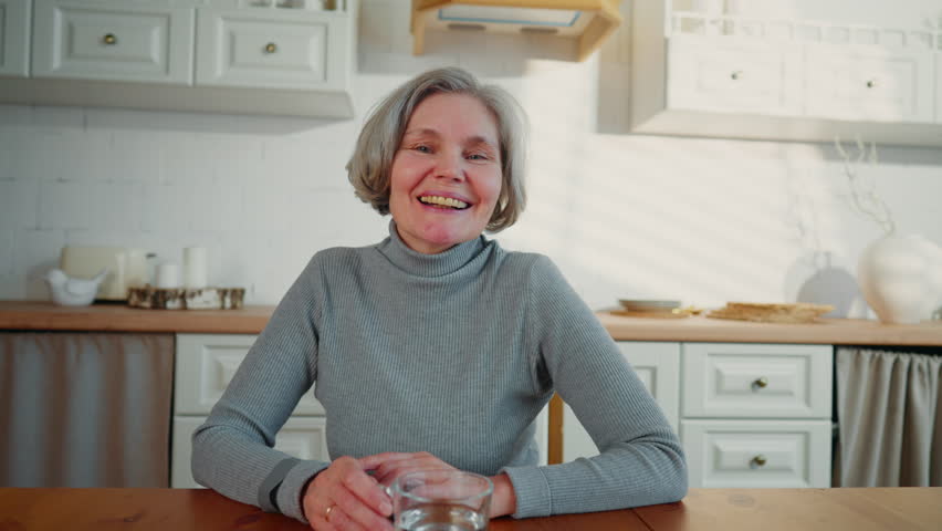 Happy senior lady smiling to camera, portrait in home interior, pretty housewife . Positive emotions and good mood, good feelings and healthcare in old age, better aging, grey-haired caucasian woman