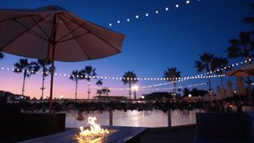 sunset terrace umbrella over waterfront string lights and fire pit reflect on calm pool, palm silhouettes - Powered by Shutterstock - Get 15% off with code: PIKWIZARD15