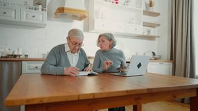 Elderly caucasian man and woman looking for information in books and in internet . Portrait of aged married couple in home kitchen, lady using laptop and man reading book, pastime, leisure in weekend - Powered by Shutterstock - Get 15% off with code: PIKWIZARD15
