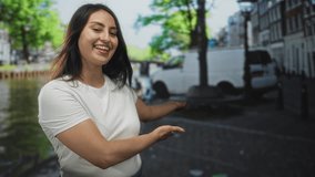 Young woman smiling, presenting with open hands on a cobblestone street by a canal in amsterdam; joyful. - Powered by Shutterstock - Get 15% off with code: PIKWIZARD15