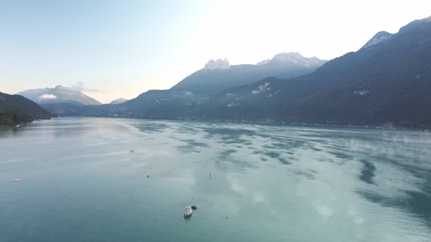 Morning mist over the water on Lake Annecy. Drone footage raises and moves forward capturing this spectacular view.