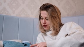 Woman in cozy white sweater looking at smartphone with calm focused expression, sitting on soft bed with cushions, relaxed indoor atmosphere, technology use blending comfort, lifestyle, communication - Powered by Shutterstock - Get 15% off with code: PIKWIZARD15