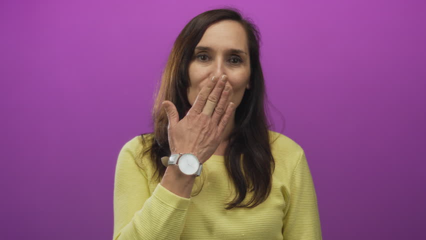 Young hispanic woman blows kiss with hand toward camera in studio; affection warmth friendliness joy.