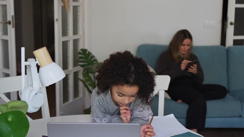 Primary school African American Student child with headphones hand writing in book using laptop. Distance learning online education. School girl studying at home with digital tablet computer and doing