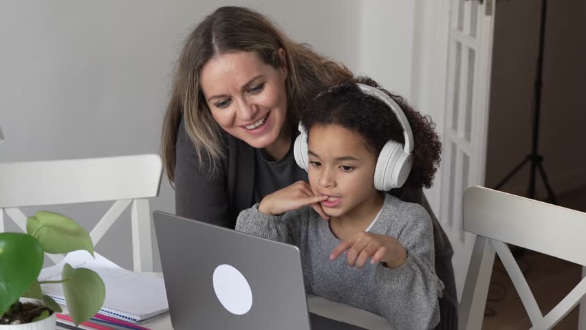Caucasian mother and African American daughter studying at home, mom teaching math doing homework in cosy white room. Parent teach, child school girl learn mathematics, write exercise read book