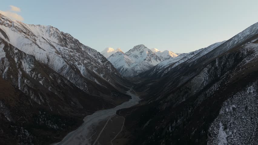 Aerial view captures the stunning snow-capped mountains and expansive valley below, showcasing the natural beauty and rugged terrain, as the camera pans smoothly across the landscape