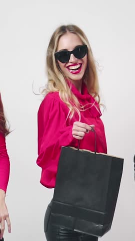 Three women smile and pose with shopping bags after a fun shopping day