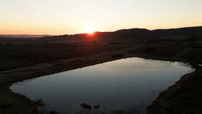 A drone view of sunrise reflecting on a tranquil pond surrounded by rural fields and rolling hills near Piriapolis, Uruguay, on a calm morning - Powered by Shutterstock - Get 15% off with code: PIKWIZARD15