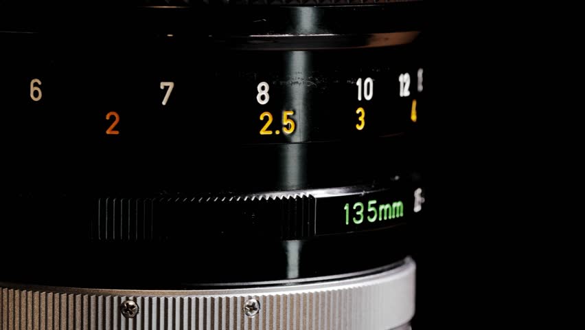 Rotating black vintage 135mm camera lens showing aperture and distance scale numbers