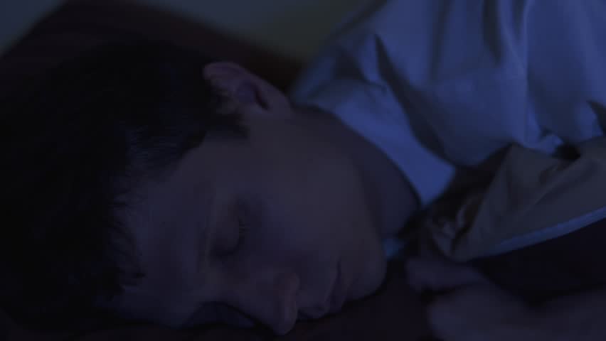 Close-up of a lonely man lying awake at night, staring into the dark with tired, empty eyes. Feeling sadness, emotional burnout and hopeless thoughts.