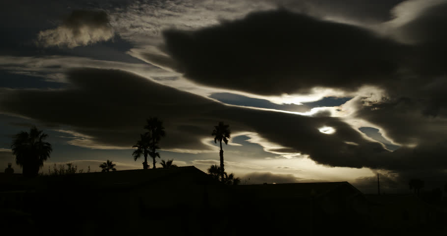 Atmospheric storm clouds haunt silhouetted house roofs and palm trees on a beautiful autumn evening.