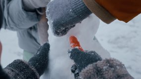 Closeup of parents and child using gloved hands to place carrot nose on snowman in snowy forest - Powered by Shutterstock - Get 15% off with code: PIKWIZARD15